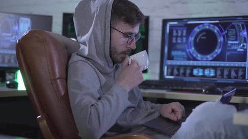Seitenansicht eines selbstbewussten kaukasischen Programmierers, der auf der Laptoptastatur tippt und nachts Kaffee trinkt