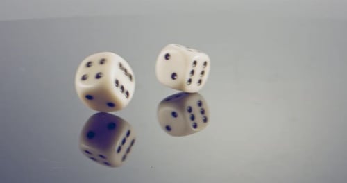 Macro disparo a cámara lenta de dados blancos cayendo y rodando sobre una superficie reflectante