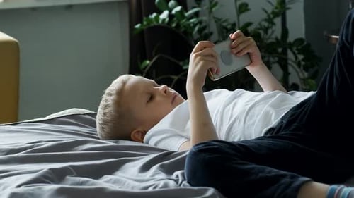 Young Boy Relaxing, Playing on Smartphone on Bed