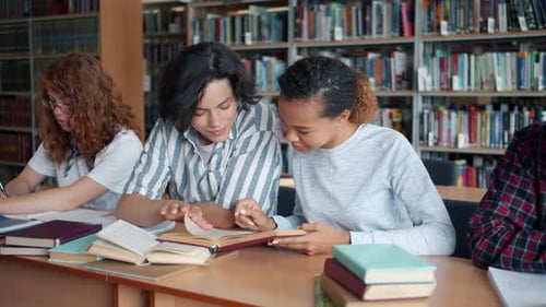 Cheerful Students Talking Reading Books in Library Making Project Together