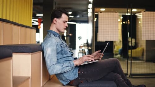 Footage of a Young Attractive Guy Sitting in an Empty Open Coworking Area Indoors with Laptop on His
