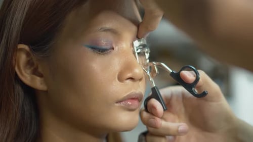 Young female model having her eyelashes curled in the makeup studio by a professional artist