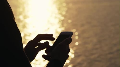 Person Using Phone at Sunset by the Ocean