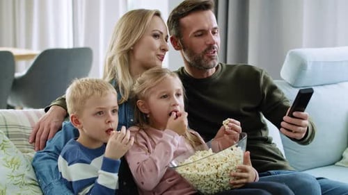 Family Relaxing on Couch Watching Television and Eating Popcorn