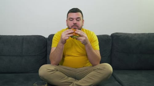 Adult Enjoys Burger Sitting on a Couch