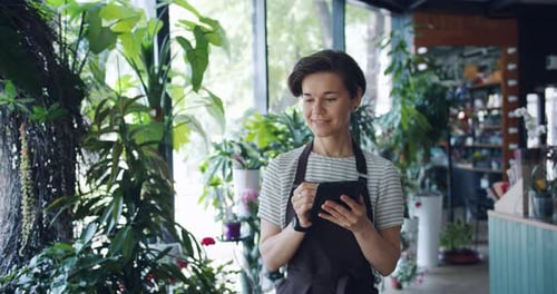 Pretty Female Florist Counting Plants Entering Records in Tablet Busy with Work