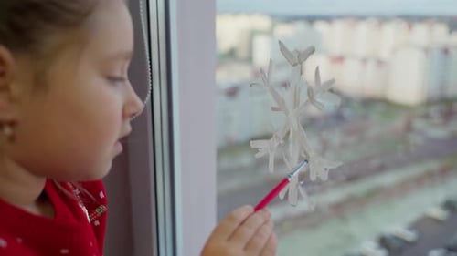 Child draw snowflake on window with paints close-up. Caucasian female person decorate living room