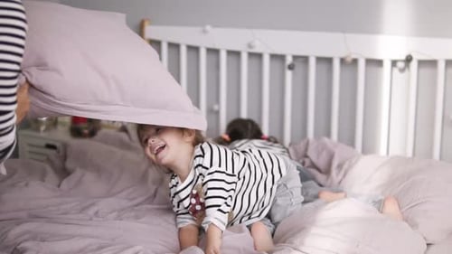 Une jolie fille heureuse avec sa sœur et sa mère ont des oreillers, se battent sur un lit rose et amusez-vous