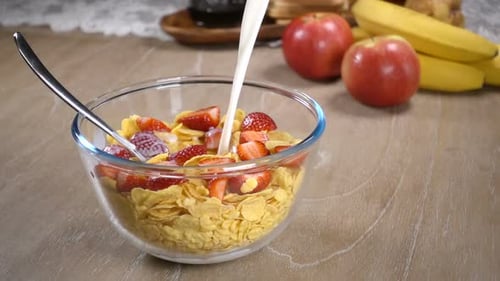 Pouring Milk on Cornflakes and Strawberries for Breakfast