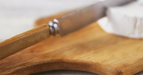 Knife Cutting Brie Cheese on Wooden Cutting Board