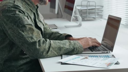 Man in Camouflage Jacket Works on Laptop