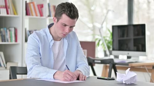 Man Writing and Crumpling Paper at Desk Indoors