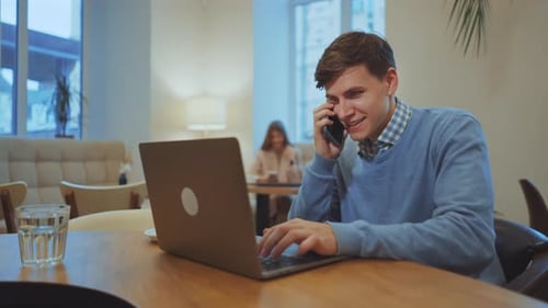 Businessman working on laptop and talking on phone in cafe