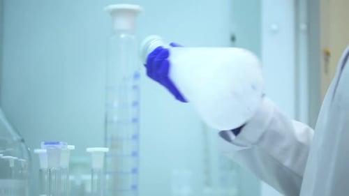 Chemiker im Chemielabor hält eine Flasche transparentes flüssiges Reagenz und schüttelt es Spbd