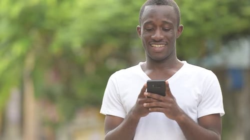 Young Man Using Smartphone and Smiling Outdoors