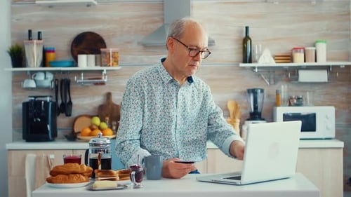 Senior Man Using Laptop in Bright Kitchen
