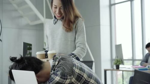 Asian businesswoman giving coffee to her colleague who is working with laptop at office