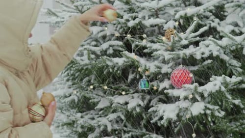 Woman Decorates Snowy Christmas Tree with Ornaments