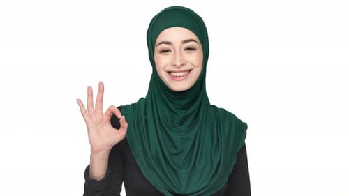 Porträt einer glücklichen muslimischen Frau der 20er Jahre mit traditionellem Kopftuch, OK-Schild mit Finger und Lächeln