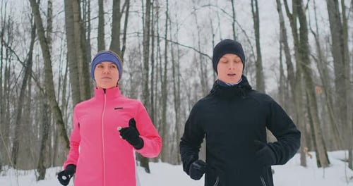 A Man and a Woman in a Pink Jacket in the Winter Running Through the Park in Slow Motion. Healthy