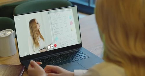 Vue arrière d'une femme caucasienne aux cheveux roux assise à son bureau à la maison et suivant un cours en ligne avec