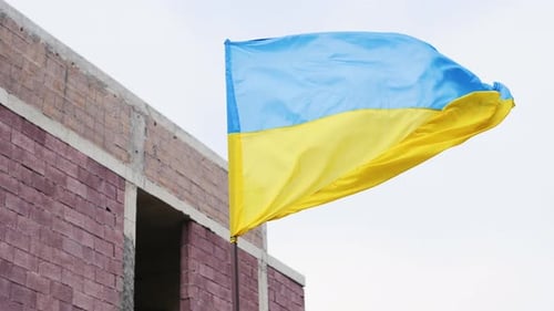 Blue and Yellow Flag Waves by Brick Building