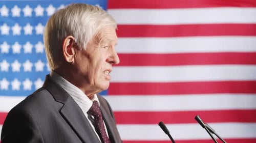 Senior Man Speaks at Podium with American Flag