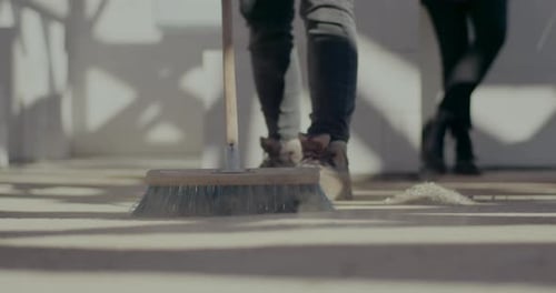 Adult Sweeping Debris on Concrete Floor
