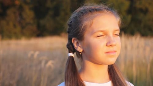Portrait of Happy Little Girl Stands at Grass Meadow Looking at Beautiful Evening Sunset