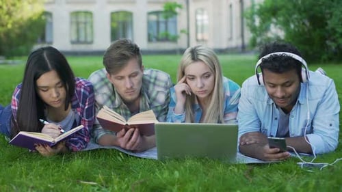 Studenten gemischter Rassen liegen auf Gras und bereiten sich auf Prüfungen vor, Hochschulbildung