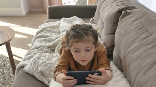 Child Plays on Smartphone Lying on Couch