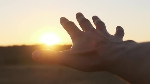 Männliche Hand gegen Sonnenuntergang. Berühre die Sonne. Die Sonne scheint durch die Finger. Zeitlupe