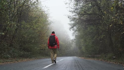 Carefree Tourist with Red Jacket Walking Calmly on Empty Foggy Road