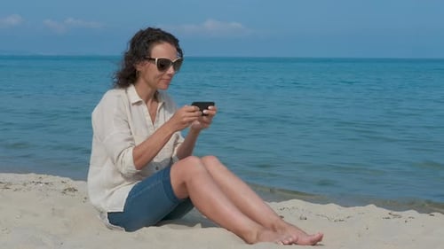 Woman plays on phone by the sea.