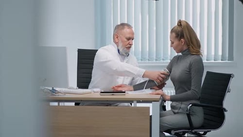 Modern Private Clinic Grayhaired Adult Male Doctor Measures the Blood Pressure of a Young Female