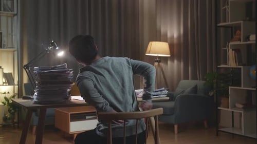 Back View Of Asian Man Having Backache While Working Hard With Documents At Home