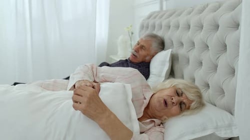 Couple de grands-parents âgés couché et dormant dans son lit. Femme perturbée par le ronflement d'un homme
