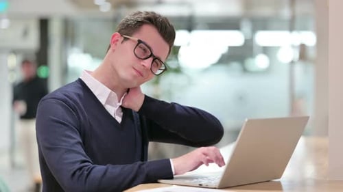 Young Man Typing, Rubbing Neck in Office