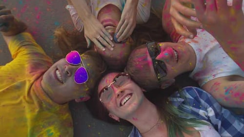 Top view of a group of friends in clothes stained with Holi colors and sunglasses, who are lying on
