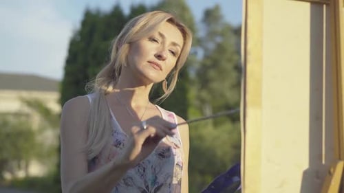 Portrait of Beautiful Blond Caucasian Woman Painting Picture Outdoors. Charming Female Artist