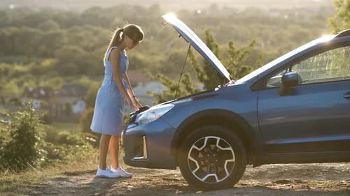Young Female Driver Standing Near a Broken Car with Open Up Hood Inspecting Her Vehicle Engine and