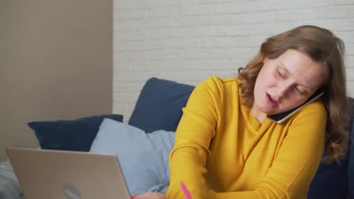 Woman Works at Laptop at Home and is in Hurry Writes Something and Talks on the Phone