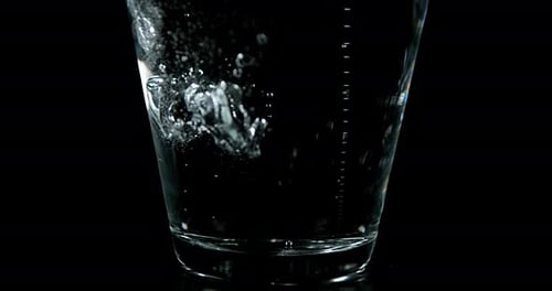 Wasser wird vor schwarzem Hintergrund in Glas gegossen, Zeitlupe 4K