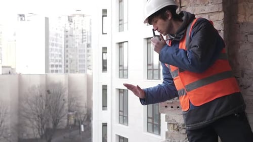 A construction engineer at a construction site controls a crane using a radio walkie-talkie.