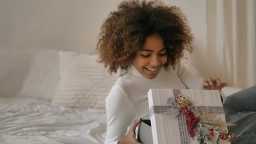 Young Woman Opening Christmas Gift on Bed