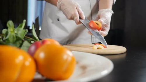 Female Chef Slicing Peach with Kitchen Knife in Slow Motion on Background. Shot with Fresh Fruit in