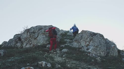 a Man and a Woman with Backpacks Climb Into the Mountains View From Below and From the Back