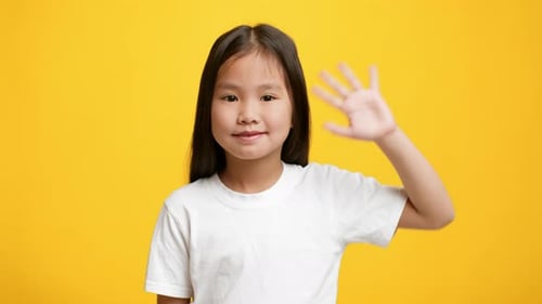 Little Korean Girl Waving Hand Gesturing Hello Over Yellow Background