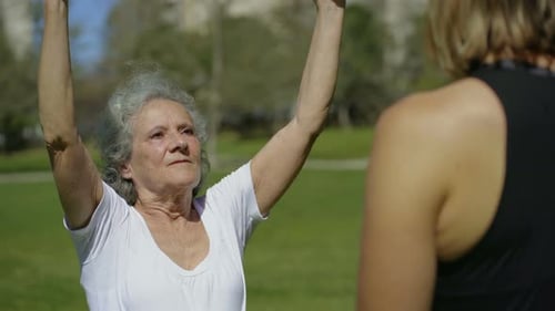 Senior Woman Exercises with Fitness Instructor in Park