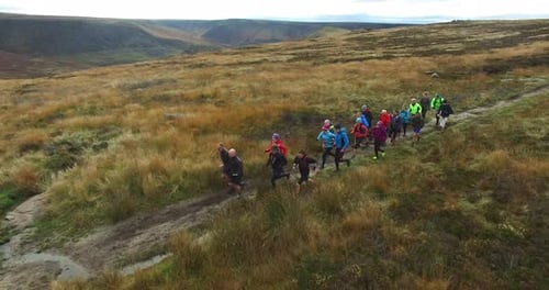 Runners Running Across Grassy Moor on Narrow Path